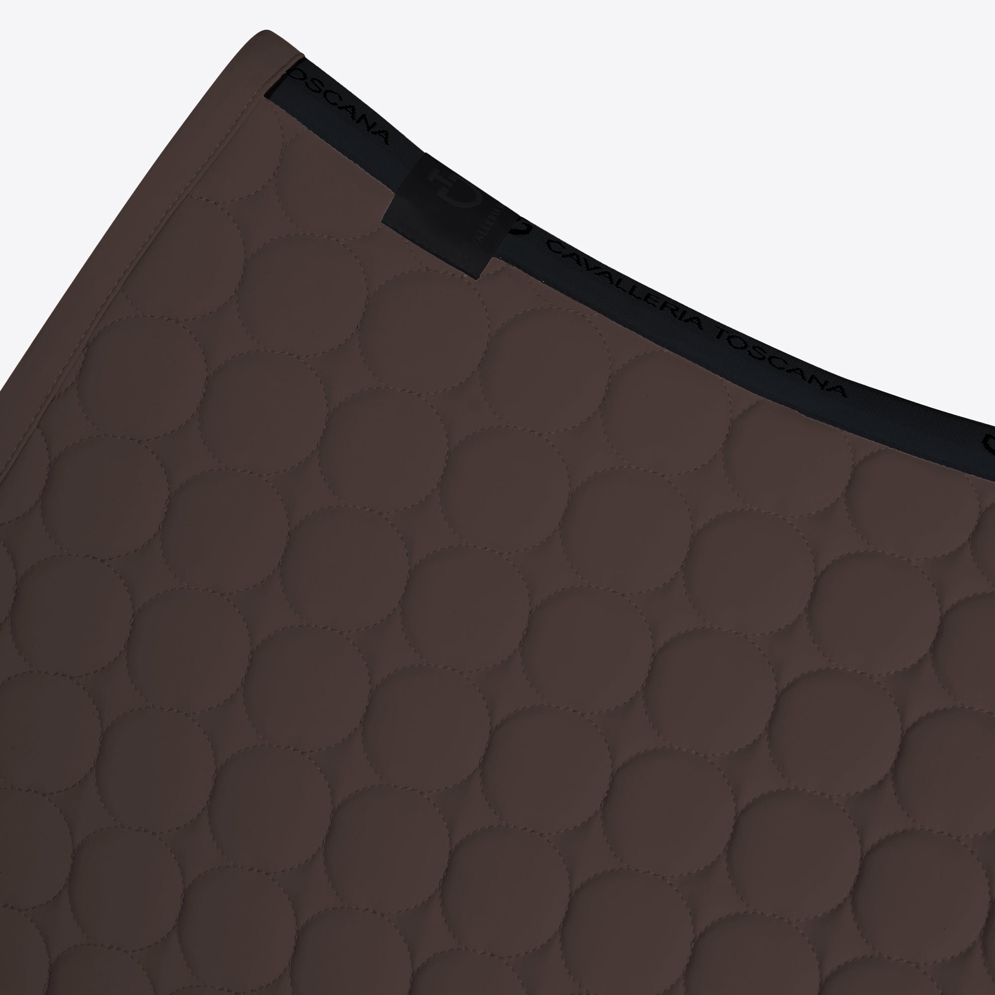 Close-up of a dark brown quilted mat with a circular stitched pattern and a black elastic trim, shown on a light gray background.