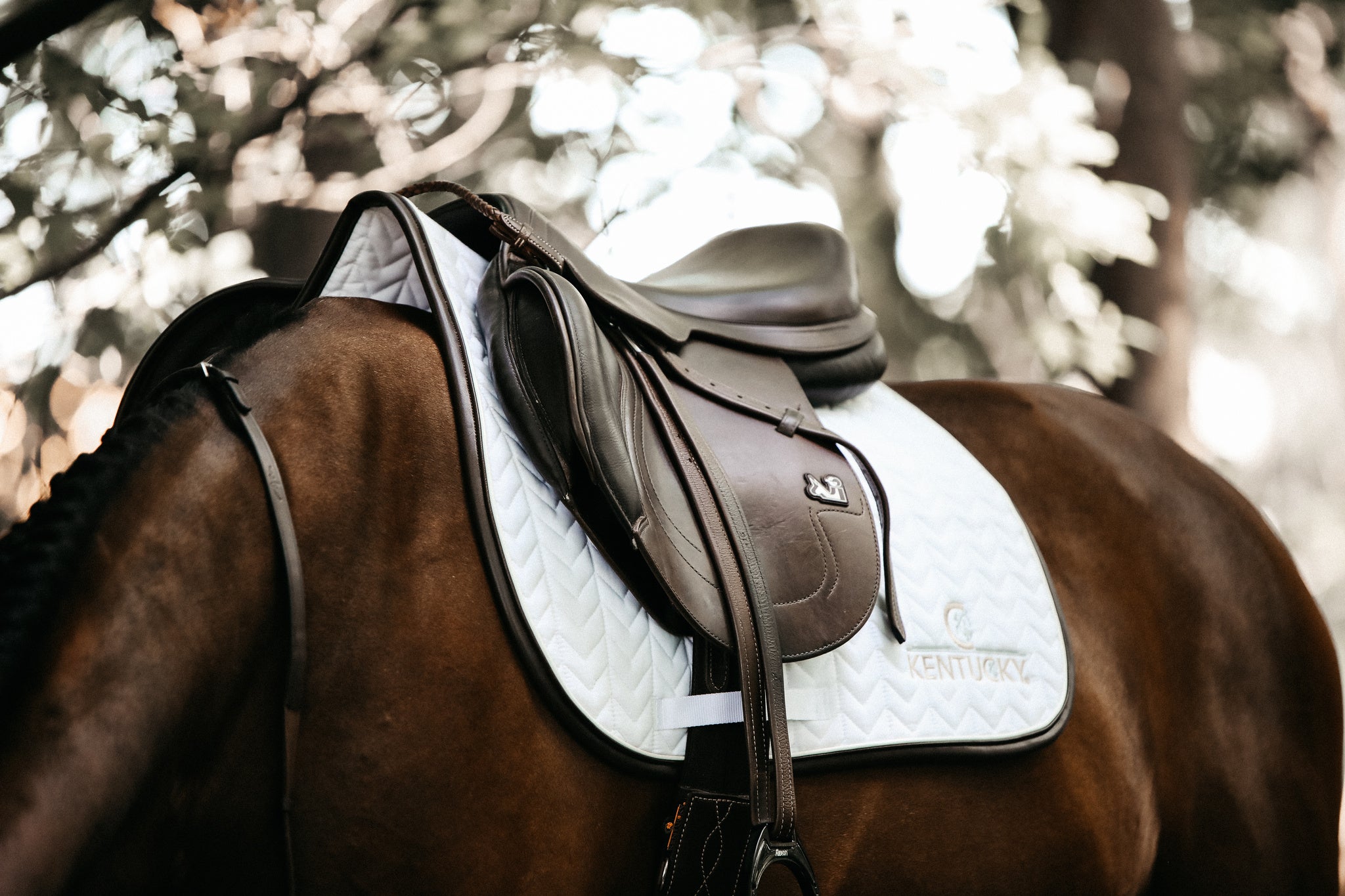 Our Saddle Pad Leather Fishbone is shaped for jumping and provides excellent cushioning between the horse’s back and the saddle while protecting against friction. This saddle pad has a unique fishbone quilting. It has no annoying straps to attach to the saddle, only a nylon strap for the girth. The Saddle Pad Leather Fishbone features a very classy leather binding and the stylish Kentucky logo