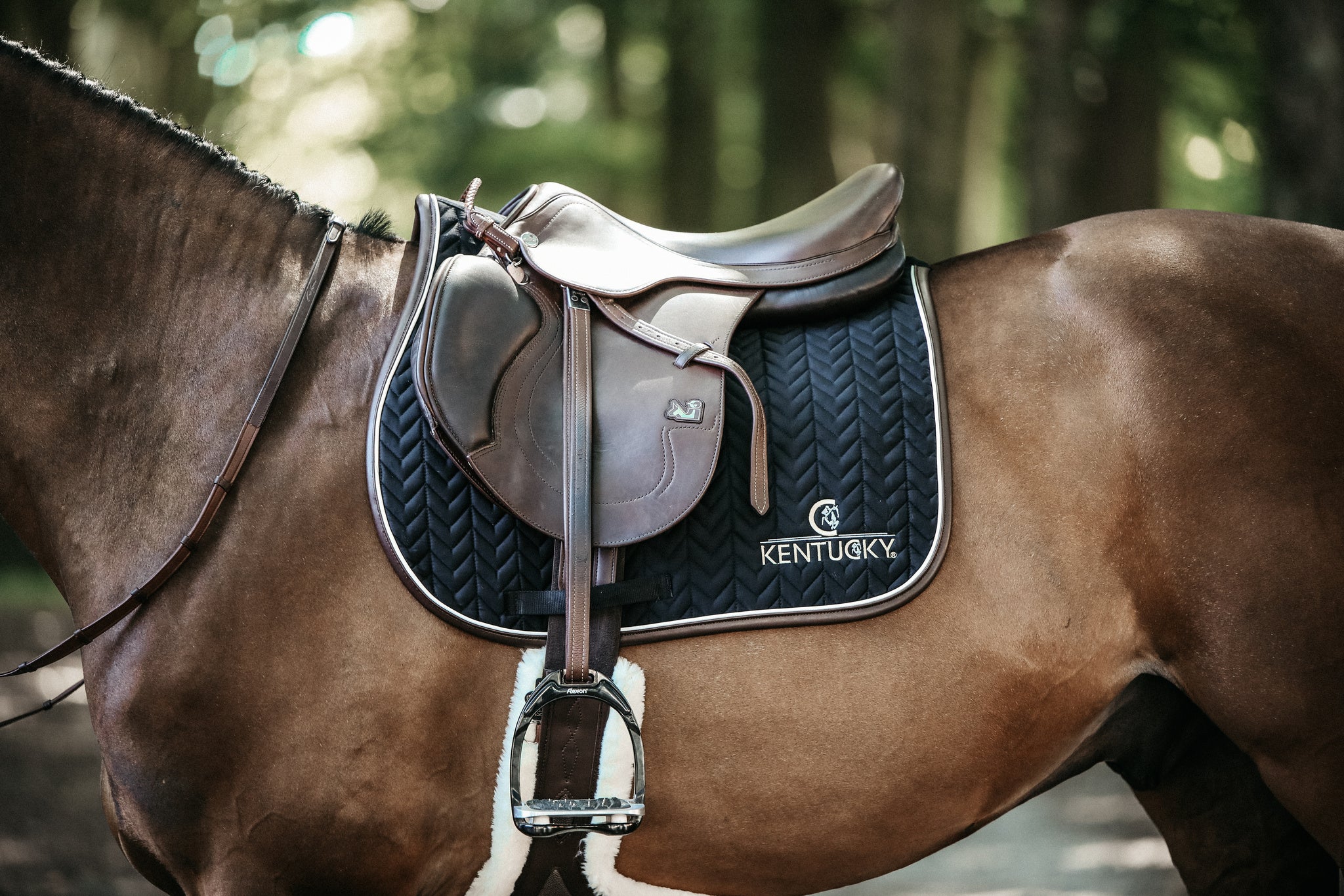 Our Saddle Pad Leather Fishbone is shaped for jumping and provides excellent cushioning between the horse’s back and the saddle while protecting against friction. This saddle pad has a unique fishbone quilting. It has no annoying straps to attach to the saddle, only a nylon strap for the girth. The Saddle Pad Leather Fishbone features a very classy leather binding and the stylish Kentucky logo