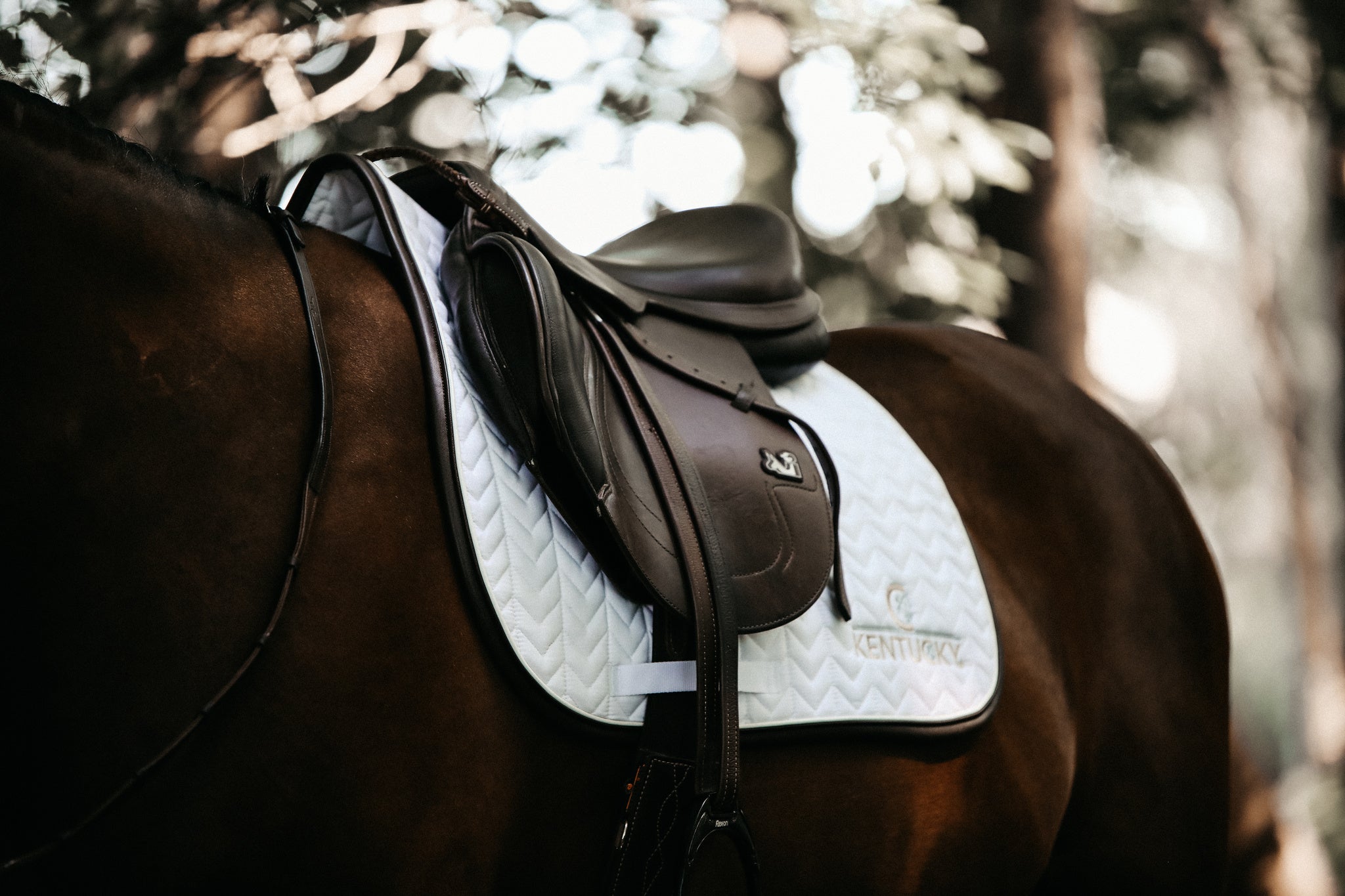 Our Saddle Pad Leather Fishbone is shaped for jumping and provides excellent cushioning between the horse’s back and the saddle while protecting against friction. This saddle pad has a unique fishbone quilting. It has no annoying straps to attach to the saddle, only a nylon strap for the girth. The Saddle Pad Leather Fishbone features a very classy leather binding and the stylish Kentucky logo