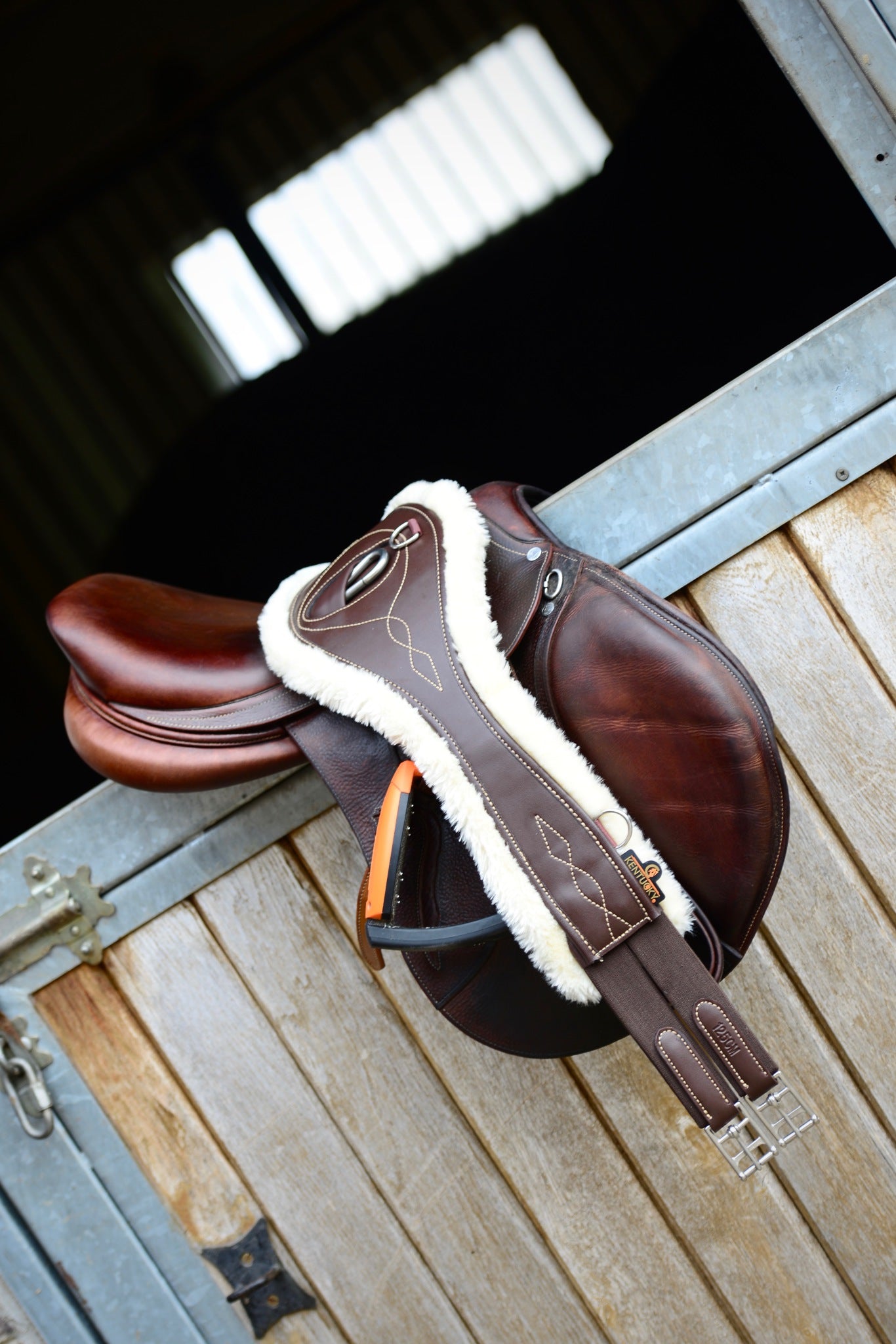 The Kentucky anatomical girth with sheepskin lining. This girth is made from artificial leather, making it softer, more durable and easier to maintain and clean. The faux sheepskin is removable, making it easier to watch and re attaches with strong Velcro. A silver hope and carabiner is found underneath to attach your martingale, breastplate, draw reigns etc. The girth is available in black or brown.