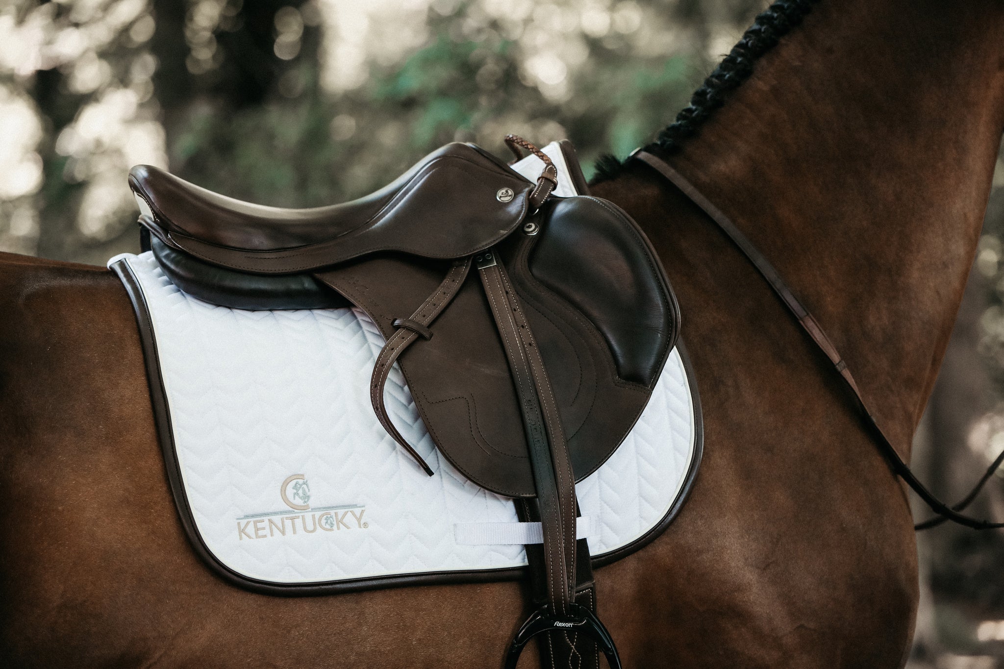 Our Saddle Pad Leather Fishbone is shaped for jumping and provides excellent cushioning between the horse’s back and the saddle while protecting against friction. This saddle pad has a unique fishbone quilting. It has no annoying straps to attach to the saddle, only a nylon strap for the girth. The Saddle Pad Leather Fishbone features a very classy leather binding and the stylish Kentucky logo