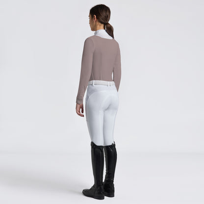 A woman shown from the back wearing a fitted taupe long-sleeve top, white riding breeches, and black equestrian boots against a clean light gray studio background.
