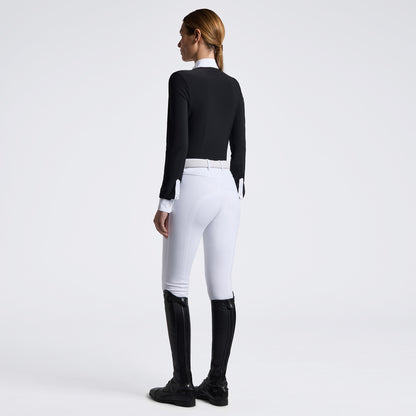 A woman shown from the back wearing a fitted black long-sleeve top, white riding breeches with a white belt, and black riding boots against a clean white studio background.
