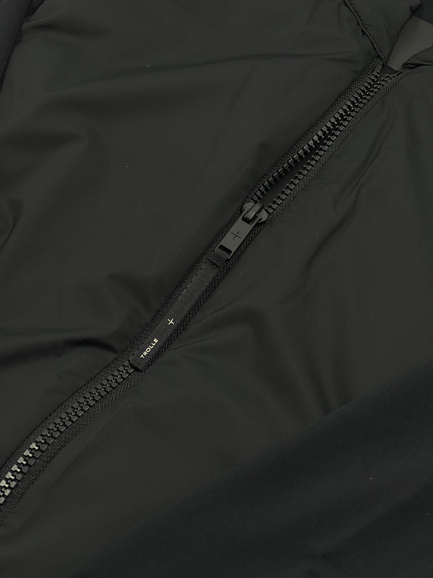 Close-up of a black jacket zipper with a brand logo.