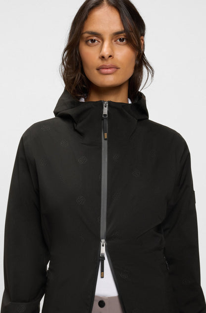 A woman wearing a black hooded jacket with a front zipper, photographed against a plain light gray studio background.