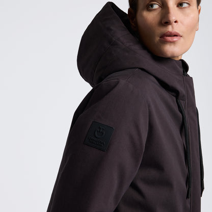 A close-up side profile of a model wearing a dark brown hooded jacket with a black rectangular logo patch on the upper sleeve, set against a plain white background.