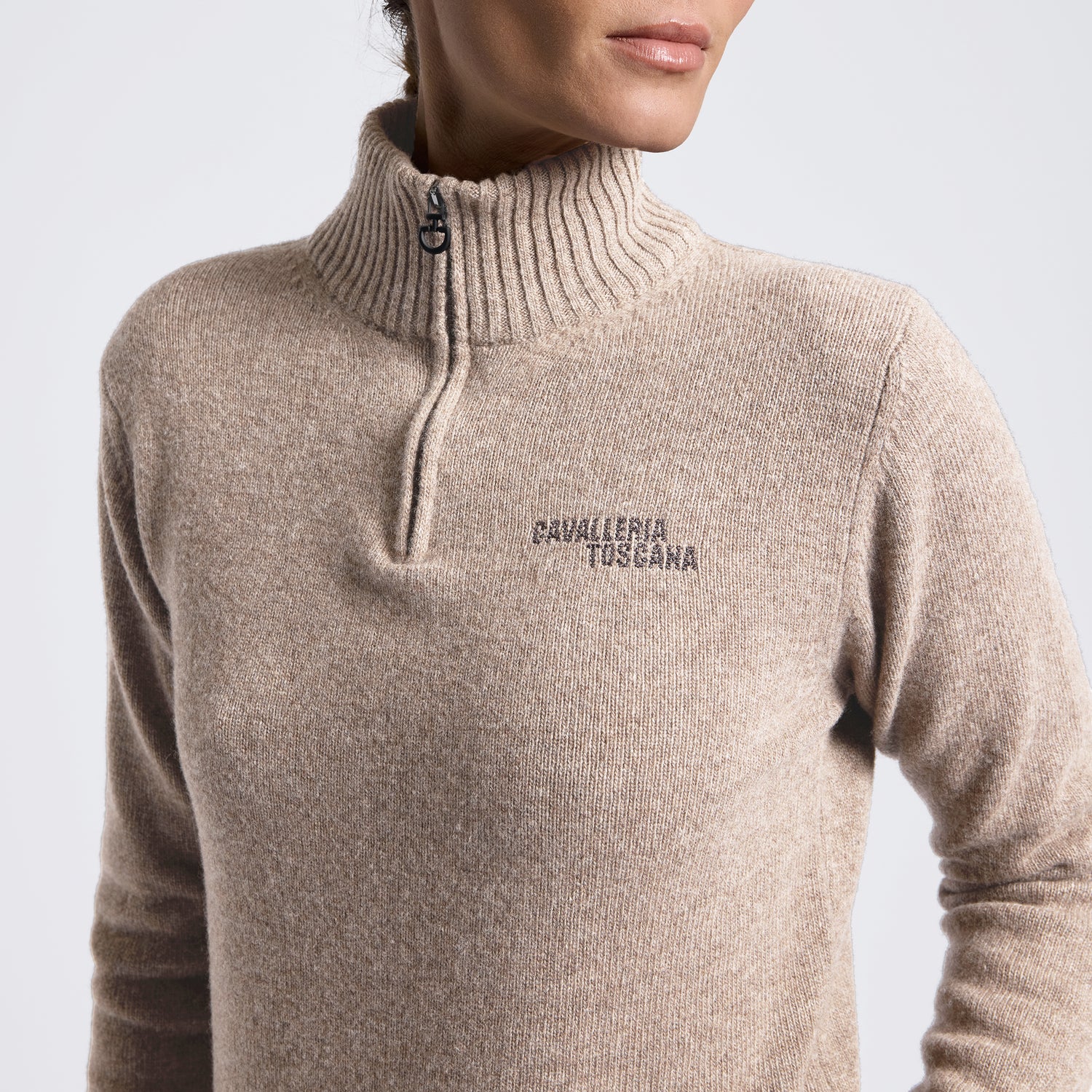 A close-up of a person wearing a beige ribbed knit quarter-zip sweater with &