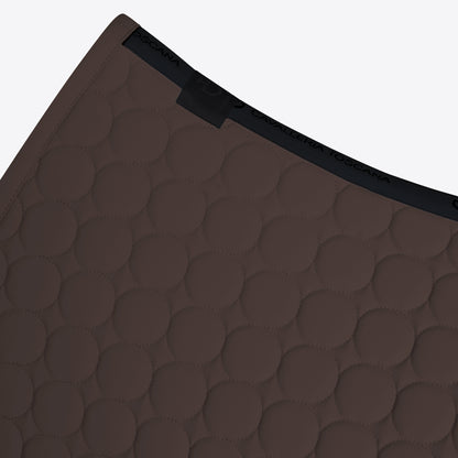 Close-up of a dark brown quilted mat with a circular stitched pattern and a black elastic trim, shown on a light gray background.