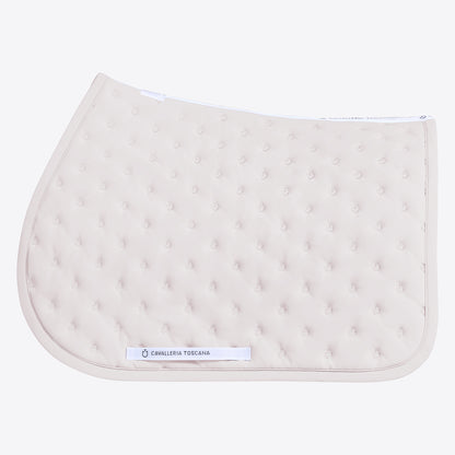 A light beige quilted equestrian saddle pad with a tufted texture and a white brand label reading &