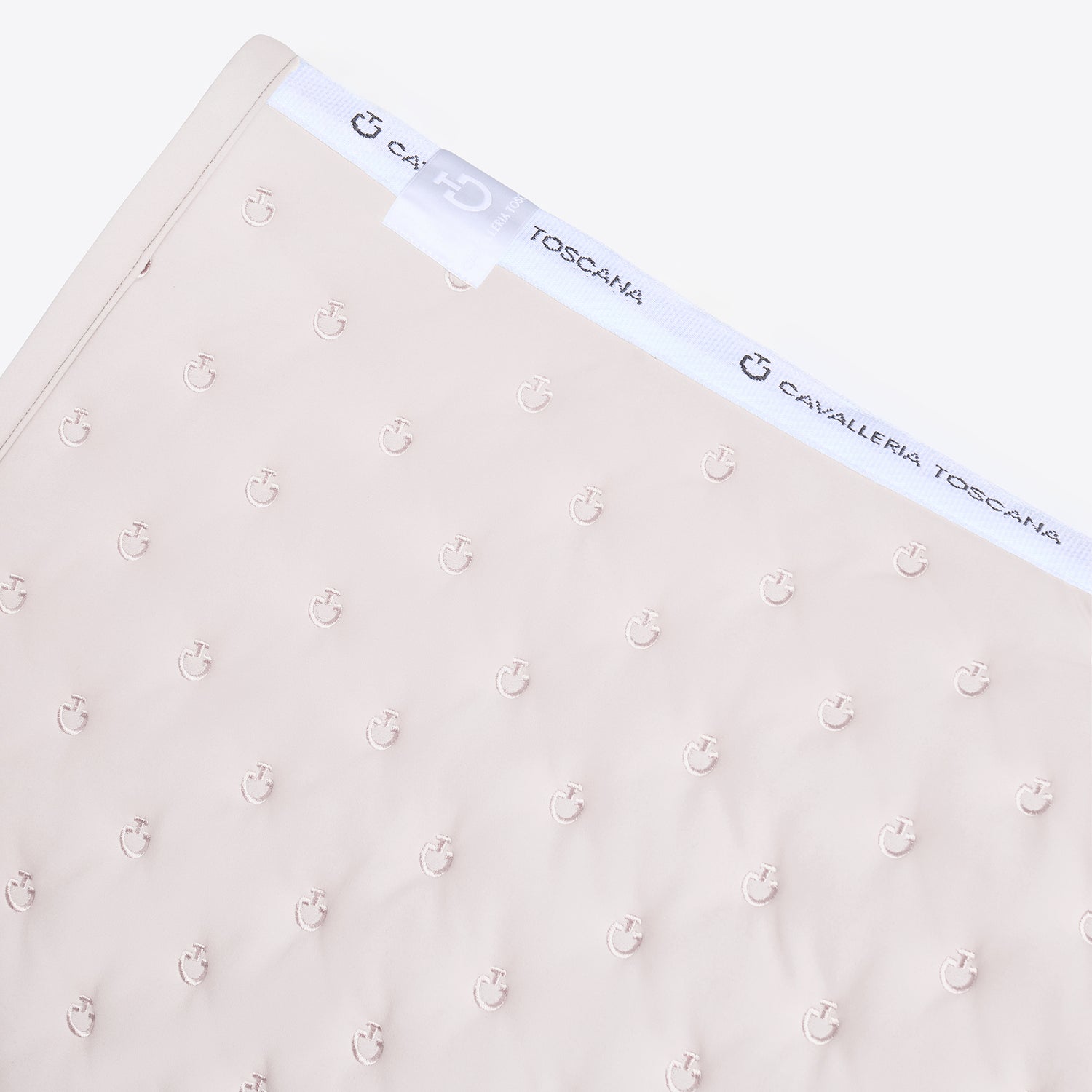 A close-up of a light beige baby blanket featuring a repeating anchor pattern and a white elastic band with the brand name &
