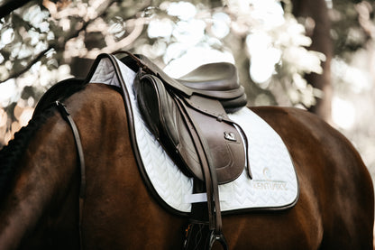 Our Saddle Pad Leather Fishbone is shaped for jumping and provides excellent cushioning between the horse’s back and the saddle while protecting against friction. This saddle pad has a unique fishbone quilting. It has no annoying straps to attach to the saddle, only a nylon strap for the girth. The Saddle Pad Leather Fishbone features a very classy leather binding and the stylish Kentucky logo
